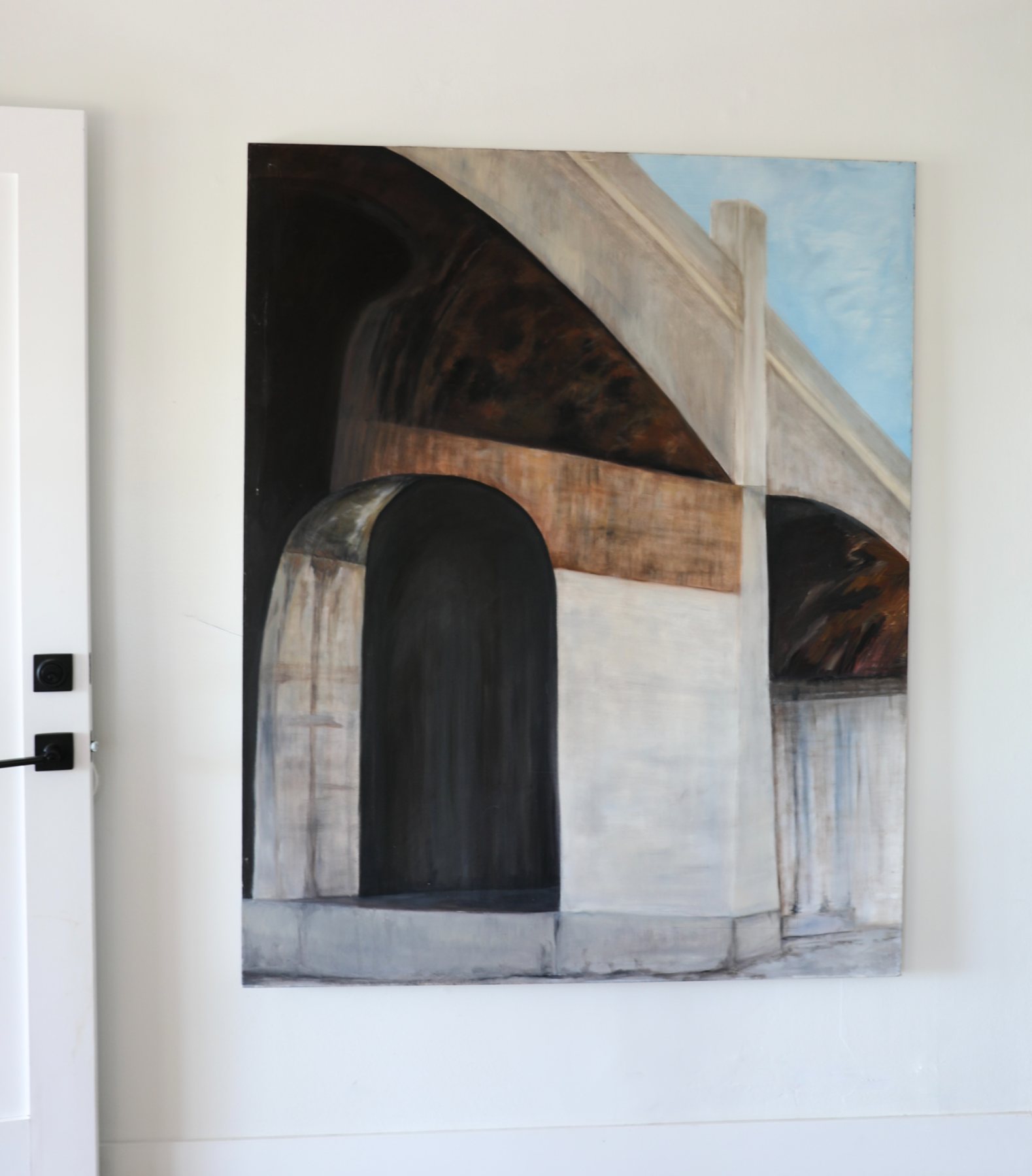 LA Bridges hanging at scale on a pale wall beside a doorway, its arches and warm ochre glowing in a bright modern room.