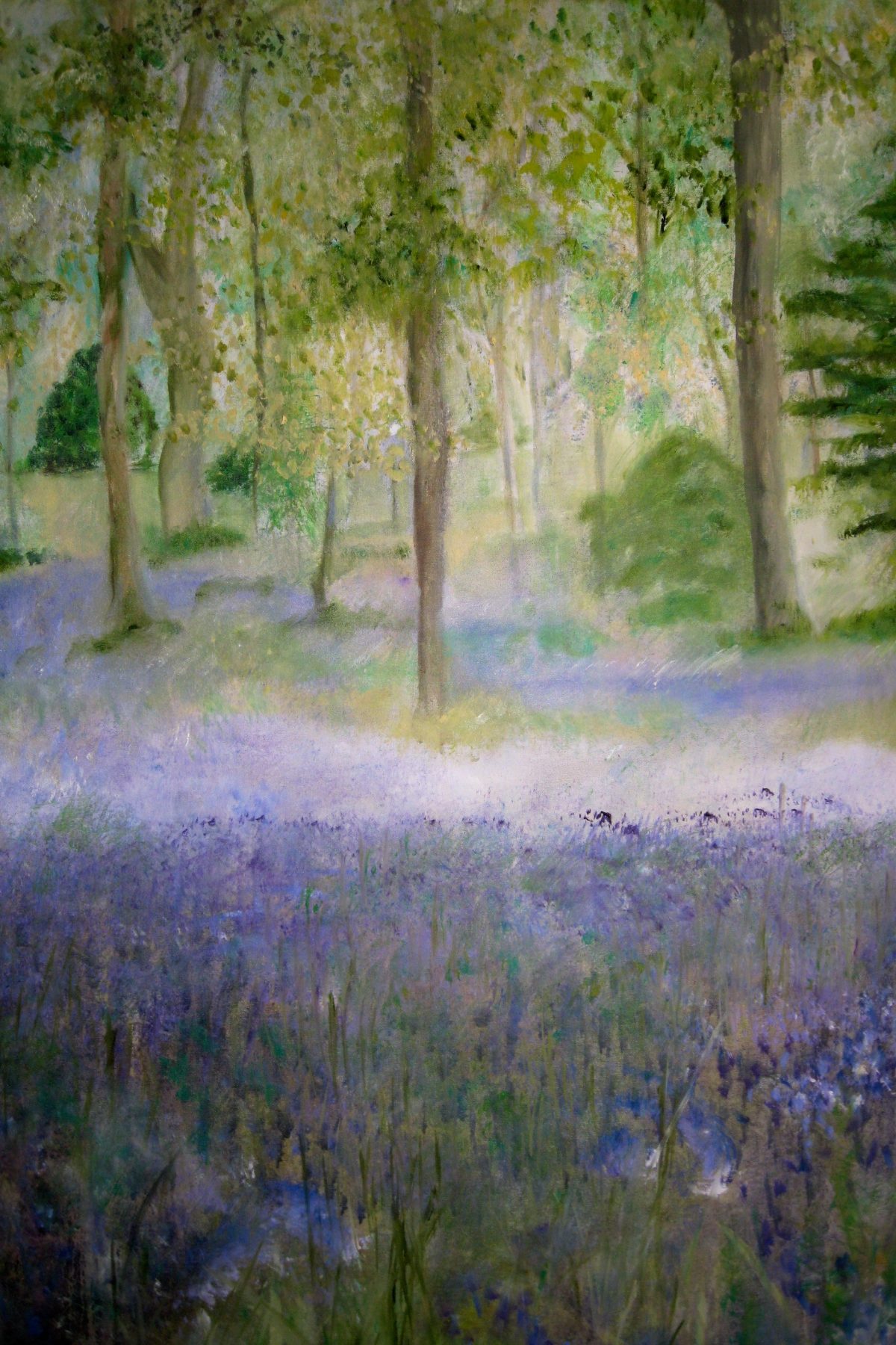 A bluebell wood, slender trees rising over a drift of violet-blue bluebells and dappled green light.
